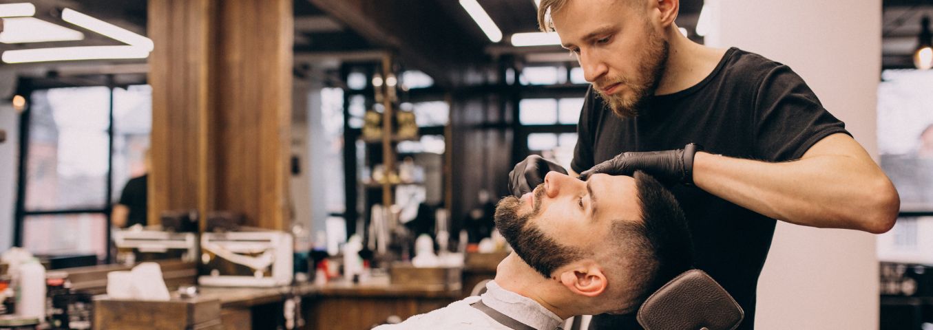 Barber realizujący usługę golenia zarostu twarzy klienta w zakładzie barberskim