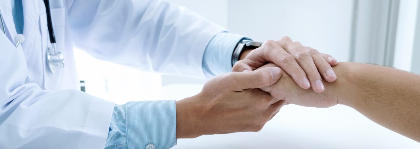 Zbliżenie na dłonie lekarza, trzymającego ze wsparciem dłoń pacjenta