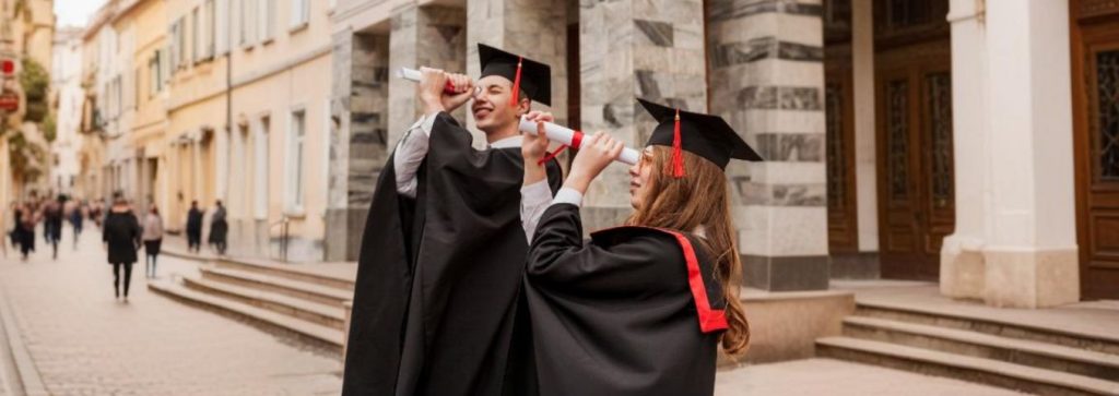 absolwenci uczelni zerkają przez zrulowane dyplomy