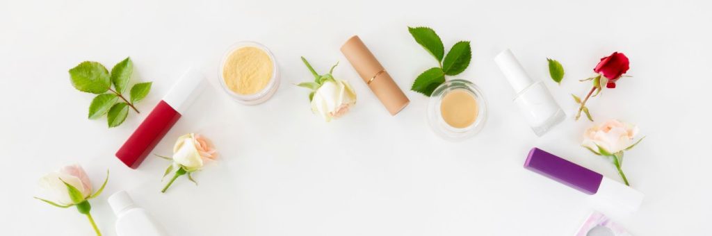 Kompozycja pąków kwiatów róży oraz liści i opakowań kosmetyków.