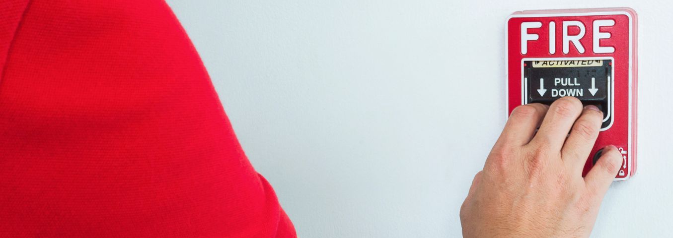 Zbliżenie na dłoń osoby uruchamiającej ręczny przycisk alarmu pożarowego